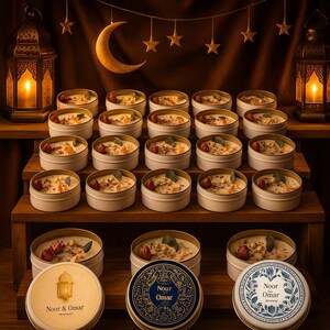 May include: A display of small, round candles in white tins, arranged on wooden shelves. Each candle is topped with decorative elements. The scene is warmly lit, with lanterns and a crescent moon adding to the ambiance. Some tins have lids with the text "Noor & Omar".