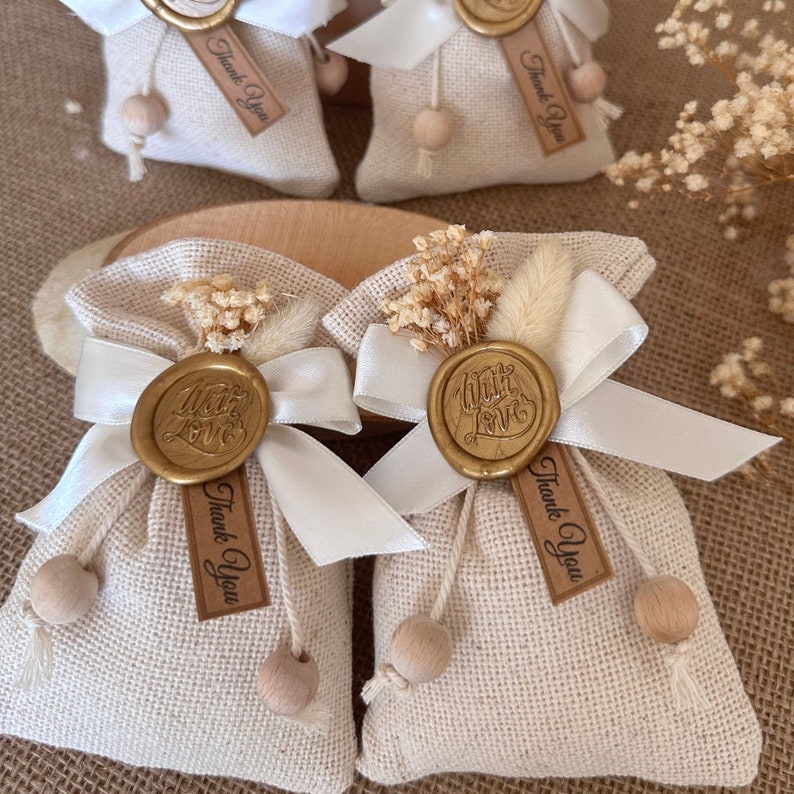 May include: Four small burlap bags with white ribbon bows and wooden beads. Each bag has a gold wax seal with the words "With Love" and a brown tag that says "Thank You".