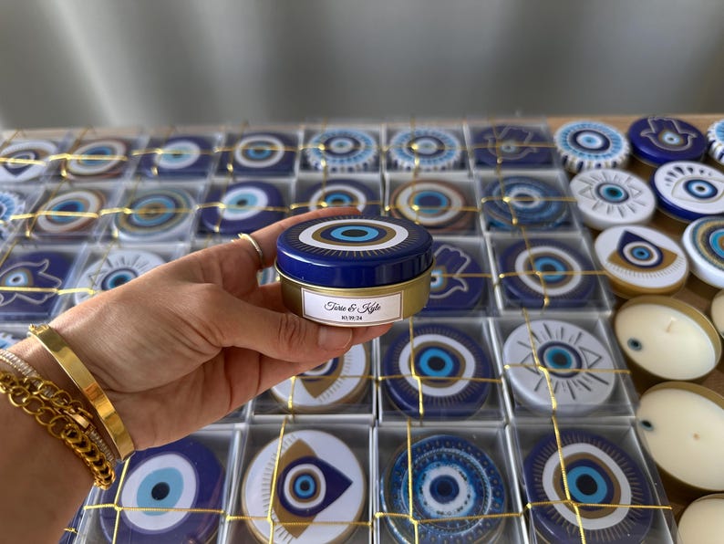 A set of different unique evil eye pattern candles, beautifully packaged in a gold string gift box. Each candle contains an evil eye bead inside, symbolizing protection, and features a personalized label for a special touch.