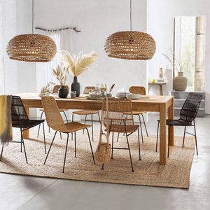 May include: A wooden dining table with six chairs, a woven rug, and two woven pendant lights. The chairs are made of black metal and woven rattan. The table is made of light brown wood. The rug is made of natural fibers.