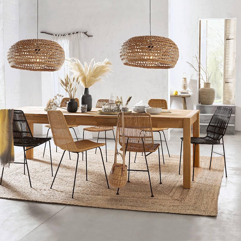 May include: A wooden dining table with six chairs, a woven rug, and two woven pendant lights. The chairs are made of black metal and woven rattan. The table is made of light brown wood. The rug is made of natural fibers.