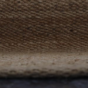 K&ouml;nnte beinhalten: Nahaufnahme eines strukturierten, gewebten Teppichs in Beige- und Braunt&ouml;nen. Die Oberfl&auml;che des Teppichs weist ein diagonales Muster mit sichtbaren Fasern und einer leicht unebenen Textur auf. Der Rand des Teppichs ist unten sichtbar.