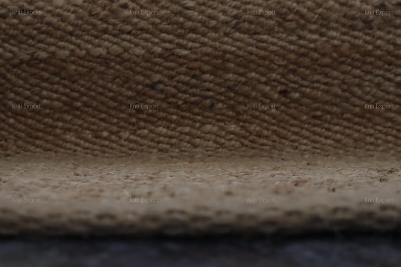 K&ouml;nnte beinhalten: Nahaufnahme eines strukturierten, gewebten Teppichs in Beige- und Braunt&ouml;nen. Die Oberfl&auml;che des Teppichs weist ein diagonales Muster mit sichtbaren Fasern und einer leicht unebenen Textur auf. Der Rand des Teppichs ist unten sichtbar.