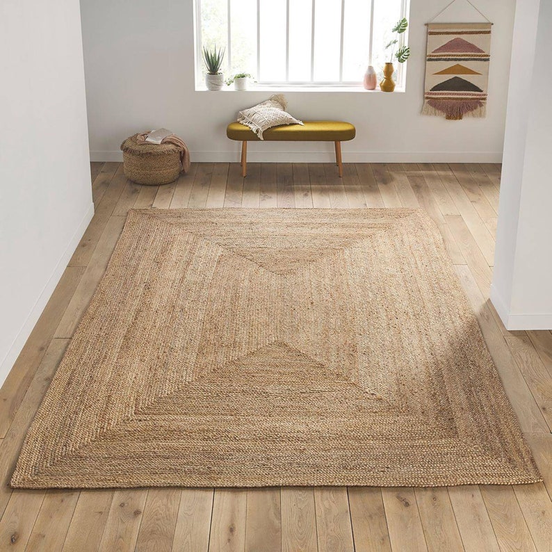 May include: A natural fiber rug with a woven design in a light brown color. The rug has a square shape with a slightly raised border.