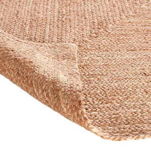 May include: Close-up of a natural fiber rug made from jute. The rug is a light brown color and has a woven texture. The rug is folded over on itself, showing the underside of the rug.