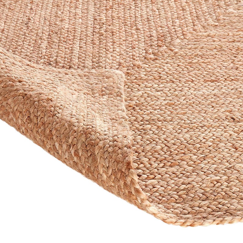 May include: Close-up of a natural fiber rug made from jute. The rug is a light brown color and has a woven texture. The rug is folded over on itself, showing the underside of the rug.