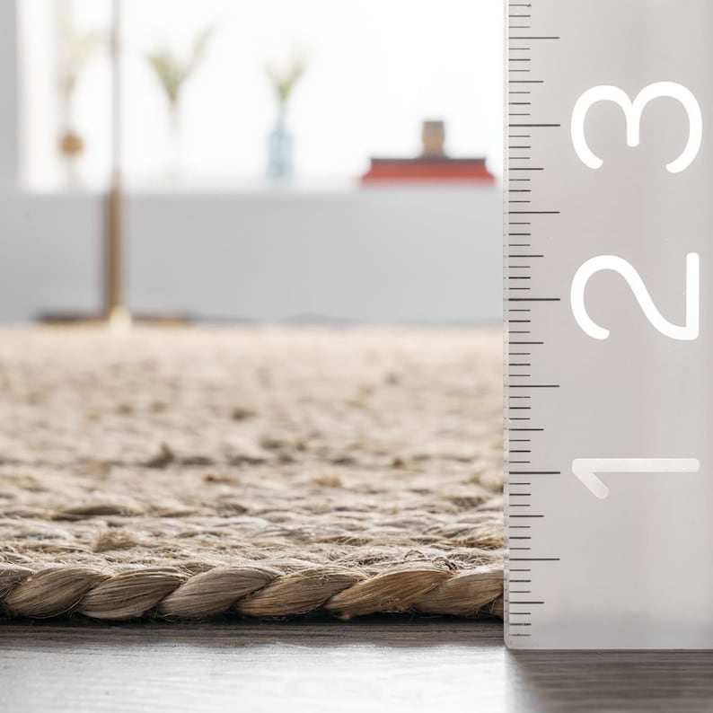 May include: Close-up of a natural fiber rug with a braided edge. A ruler with the numbers 1, 2, and 3 is visible on the right side of the image.