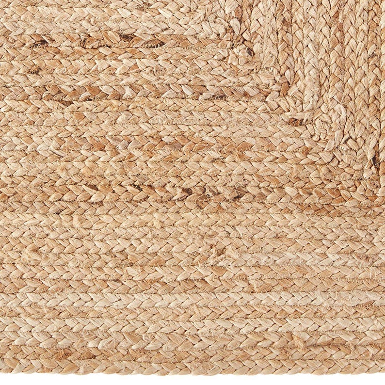 May include: A close-up of a natural fibre rug with a woven texture. The rug is made of jute and has a light brown colour.