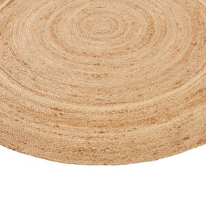 May include: A round, natural jute rug with a woven texture. The rug is a light brown color and has a circular shape.