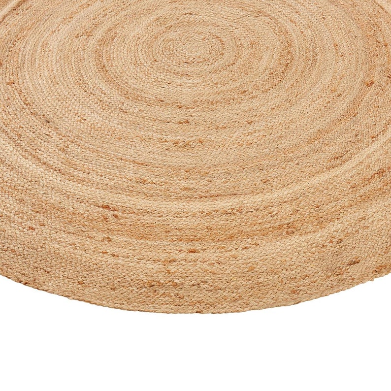 May include: A round, natural jute rug with a woven texture. The rug is a light brown color and has a circular shape.