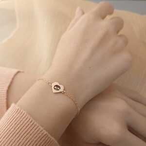May include: A delicate gold chain bracelet with a heart-shaped pendant featuring a yin yang symbol.