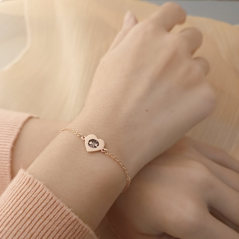 May include: A delicate gold chain bracelet with a heart-shaped pendant featuring a yin yang symbol.