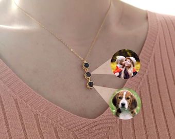 May include: A gold necklace with three round black stones hanging from it. The necklace is worn by a person with a pink sweater. There are two photos in the background, one of a woman and a child, and one of a beagle dog.