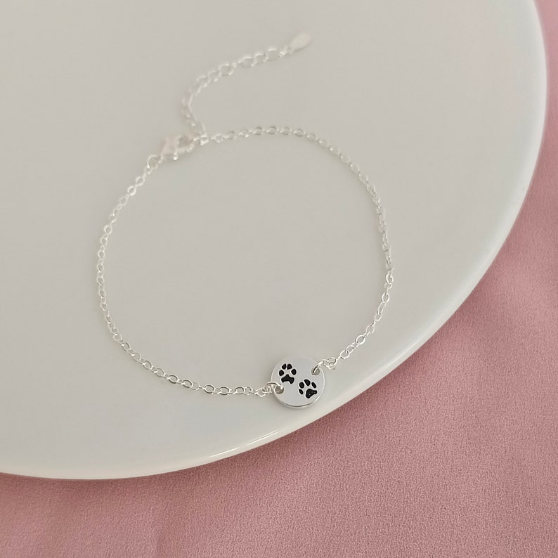 May include: A silver chain bracelet with a small round charm featuring three paw prints.