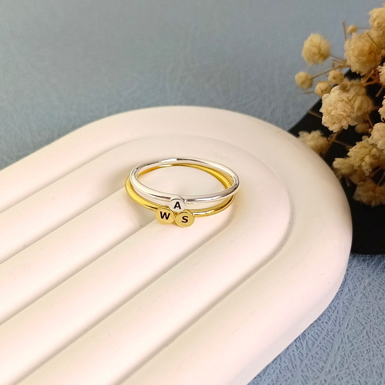 May include: Two thin gold and silver rings with the letters "W", "A", and "S" on them. The rings are stacked on top of each other.
