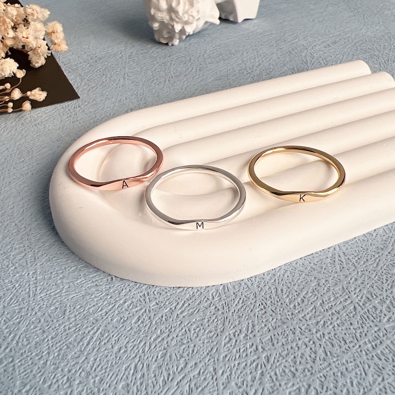 May include: Three thin, minimalist rings with engraved letters. The rings are in rose gold, silver, and gold. The letters are A, M, and K.
