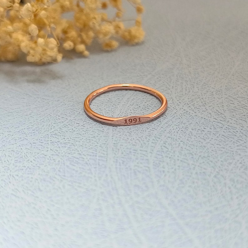 May include: A thin rose gold band ring with the year 1991 engraved on the front.
