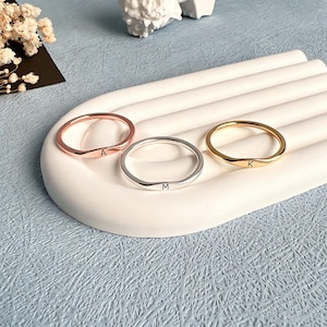 Op de afbeelding: Drie dunne metalen ringen met een glad, afgerond bandontwerp. Eén ring is roségoud met de letter A, één is zilverkleurig met de letter M en één is goudkleurig met de letter K. Elke ring heeft een klein, plat, gecentreerd plaatje met een letter.