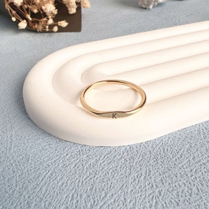 May include: A gold-colored ring with a simple, rounded design. The ring has the letter "K" engraved on the band.