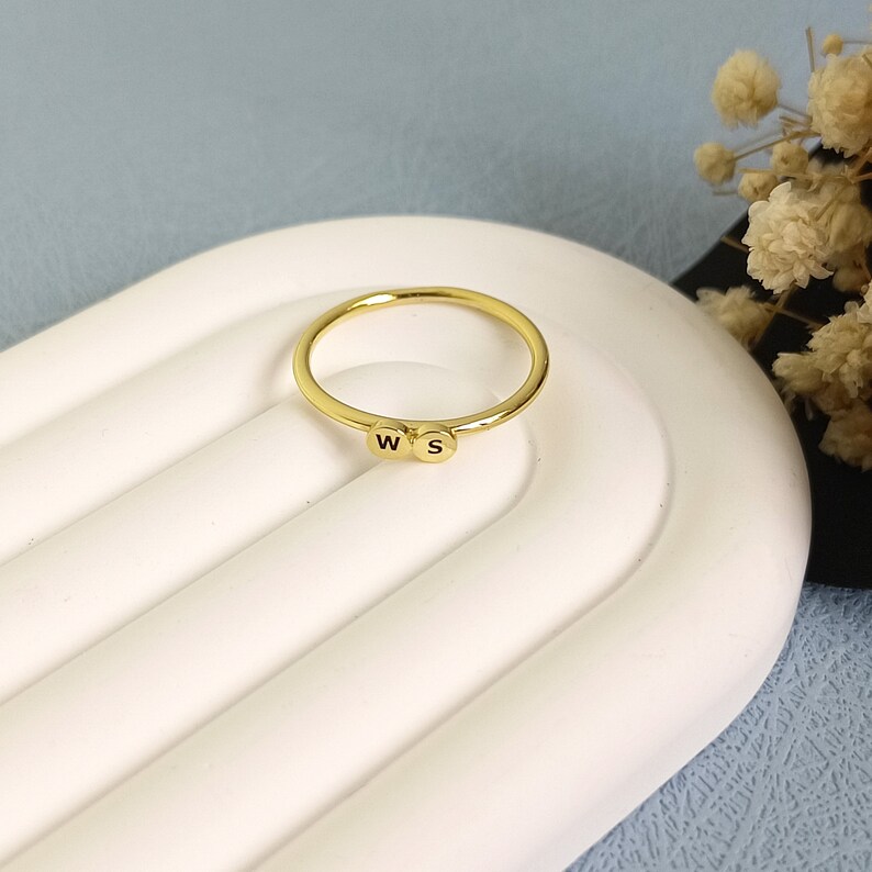 May include: A gold ring with two small round beads, each with a letter engraved on them. The letters are "W" and "S".