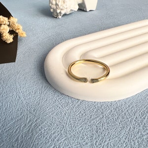 May include: A gold-toned ring with the letters "Z" and "S" engraved on the sides. The ring is on a white, curved surface.