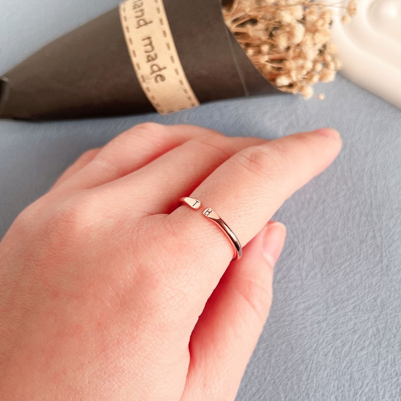 May include: A rose gold ring with a simple design. The ring has a small, engraved letter 'H' on each side of the opening.
