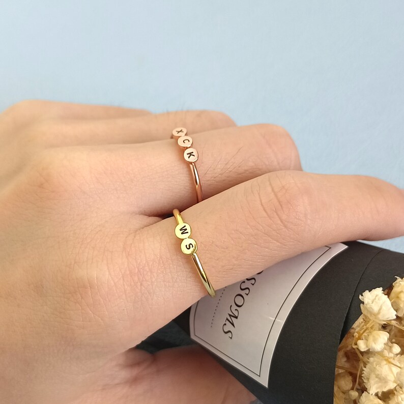 May include: Two gold rings with initial charms. The top ring has the letters "XCK" and the bottom ring has the letters "WS".