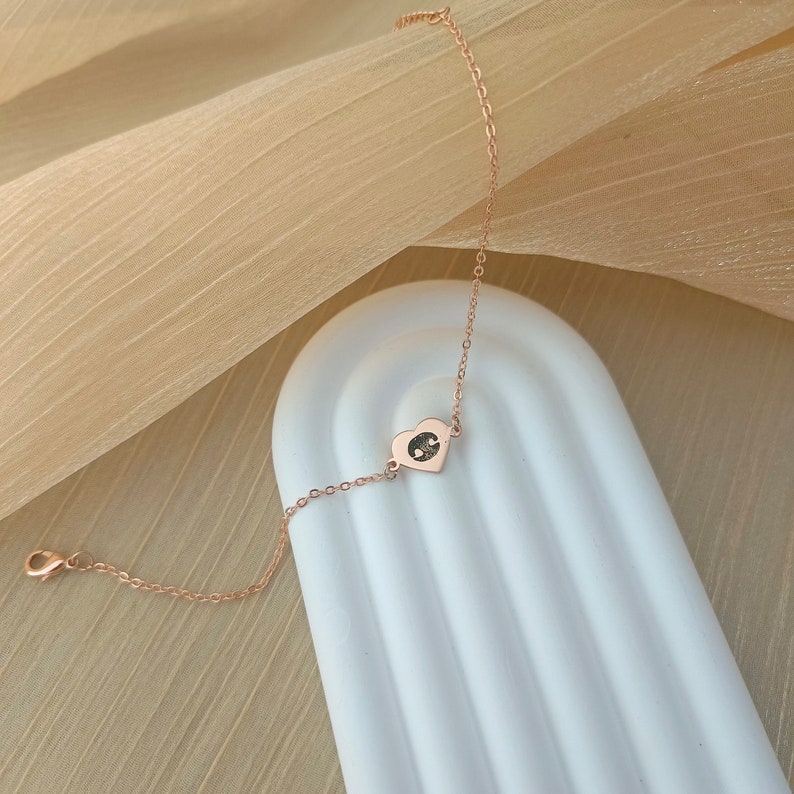 May include: A delicate rose gold chain bracelet with a small heart charm featuring a footprint design.