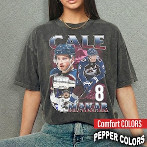 May include: A charcoal grey vintage-wash t-shirt featuring a graphic print of hockey player Cale Makar. The design includes the text CALE MAKAR, the number 8, and images of the player in a blue jersey, along with a silver trophy illustration.