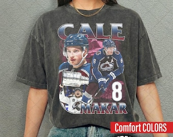 May include: A charcoal grey vintage-wash t-shirt featuring a graphic print of hockey player Cale Makar. The design includes the text CALE MAKAR, the number 8, and images of the player in a blue jersey, along with a silver trophy illustration.