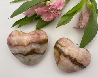 May include: Two heart-shaped polished stones with brown and pink stripes. The stones are made of banded agate.
