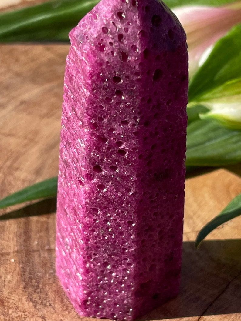 Puede incluir: Una punta de cristal de color morado oscuro con una superficie texturizada. El cristal tiene una punta puntiaguda y una base plana.