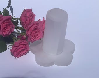 Könnte beinhalten: Ein Flaschenverschluss aus mattiertem Glas mit blütenförmigem Sockel. Links vom Verschluss ist ein Strauß rosa Rosen angeordnet. Der Verschluss ist zylindrisch und hat eine matte Oberfläche.