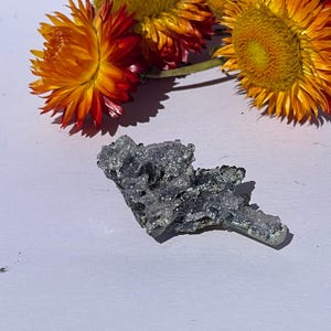 Może przedstawiać: Gromada szarych i srebrnych kryształów o szorstkiej, naturalnej fakturze. Kryształy są ułożone w nieregularny, ząbkowany kształt.