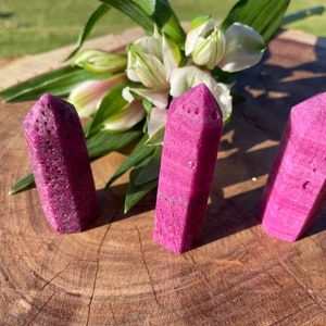 May include: Three pink crystal points with a rough, textured surface. The points are arranged in a row on a wooden surface.
