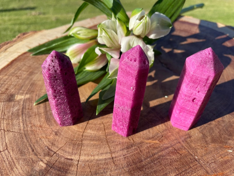 Puede incluir: Tres puntas de cristal rosa con una superficie rugosa y texturizada. Las puntas est&aacute;n dispuestas en fila sobre una superficie de madera.