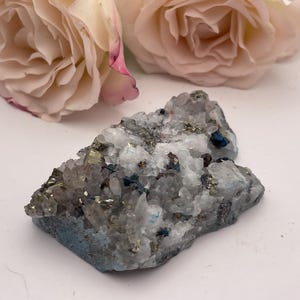 May include: A cluster of white quartz crystals with embedded pyrite and other minerals. The crystals are arranged in a rough, natural shape.