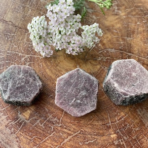 May include: Three hexagonal shaped purple ruby crystals on a wooden surface.