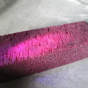 May include: A close-up of a large, rectangular, dark pink, porous stone. The stone has a rough, textured surface and appears to be made of many small, individual pieces.
