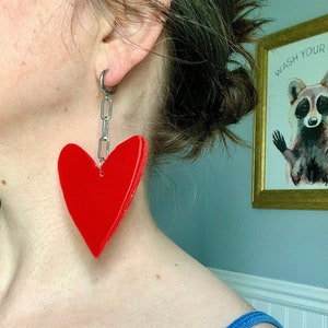 May include: A pair of red heart-shaped earrings with a silver chain hanging from each earring.