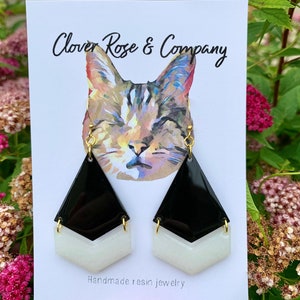 K&ouml;nnte beinhalten: Schwarze und wei&szlig;e geometrische Harzohrringe mit goldenen Haken. Die Ohrringe werden auf einer wei&szlig;en Karte mit dem Text "Clover Rose & Company" und "Handgefertigte Harzschmuck" pr&auml;sentiert.