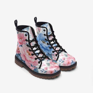 May include: A pair of floral print combat boots. The boots feature a white background with pink and blue floral patterns. They have black laces, a black pull tab, and a brown sole. The boots are designed for all-weather use.