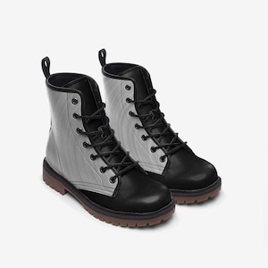 May include: A pair of ankle-high boots featuring a two-tone design with black leather-like toe caps, heels, and lace-up panels contrasted by light gray side panels with a subtle vertical ribbed texture, black laces, and brown lugged soles.