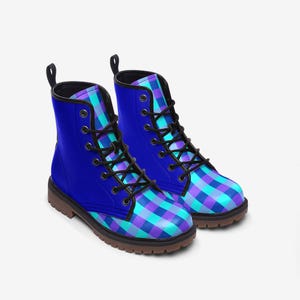 May include: A pair of ankle-high lace-up boots featuring a solid royal blue outer panel and a vibrant checkered pattern in shades of purple, cyan, and blue on the toe and tongue. The boots have black laces, black eyelets, and a brown lugged sole.