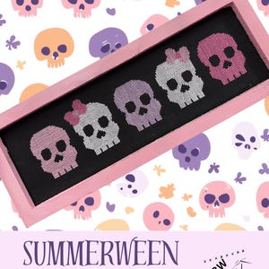 Puede incluir: Un bordado a punto de cruz enmarcado con seis diseños de calaveras coloridas en rosa, morado y blanco sobre un fondo negro. El marco es rosa y el fondo tiene un patrón repetido de calaveras en varios colores. Se muestra el texto "SUMMERWEEN SKULLS".