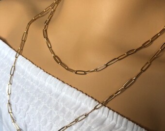 Könnte beinhalten: Zwei goldene Kettenhalsbänder mit einem Papierclip-Glied-Stil. Die Halsbänder sind auf einem weißen Hemd übereinander gelegt.