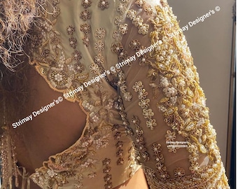May include: Ivory-colored blouse with intricate gold and pearl embroidery. The sheer sleeves are adorned with floral and leaf patterns, and the bodice features detailed beadwork. The back of the blouse has a keyhole design. The blouse is from Strimay Designer's.