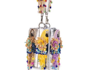 May include: Silver handbag with a rectangular shape and a silver handle. The bag is adorned with three parrot figures, each with colorful beaded details and flower accents. The handle features beaded fringe.