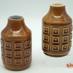 Könnte beinhalten: Zwei braune Keramikvasen mit geometrischem Muster. Die Vasen sind etwa 13 cm hoch und haben ein quadratisches Design.