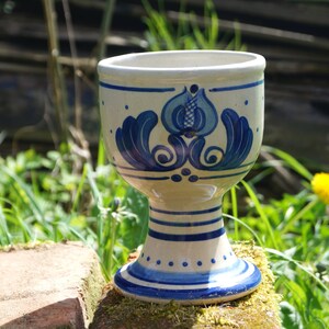 Könnte beinhalten: Eine weiße Keramiktasse mit einem blauen und weißen Blumenmuster. Die Tasse hat einen breiten Boden und eine abgerundete Oberseite.